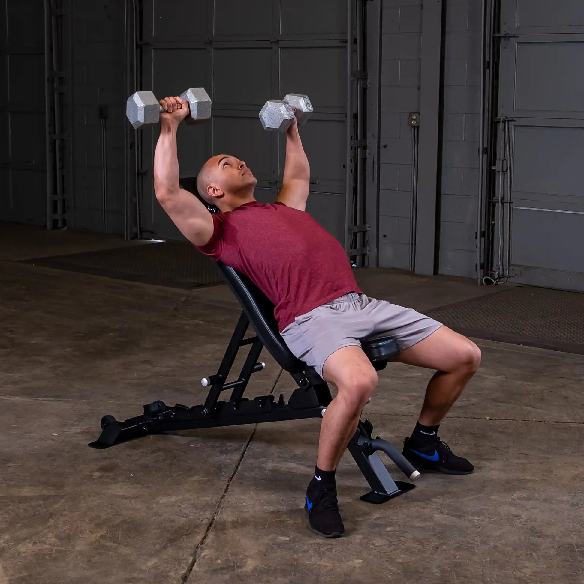 A person performing a chest press exercise using dumbbells while seated on a Body-Solid Pro ClubLine Adjustable Bench SFID325 in a gym setting.