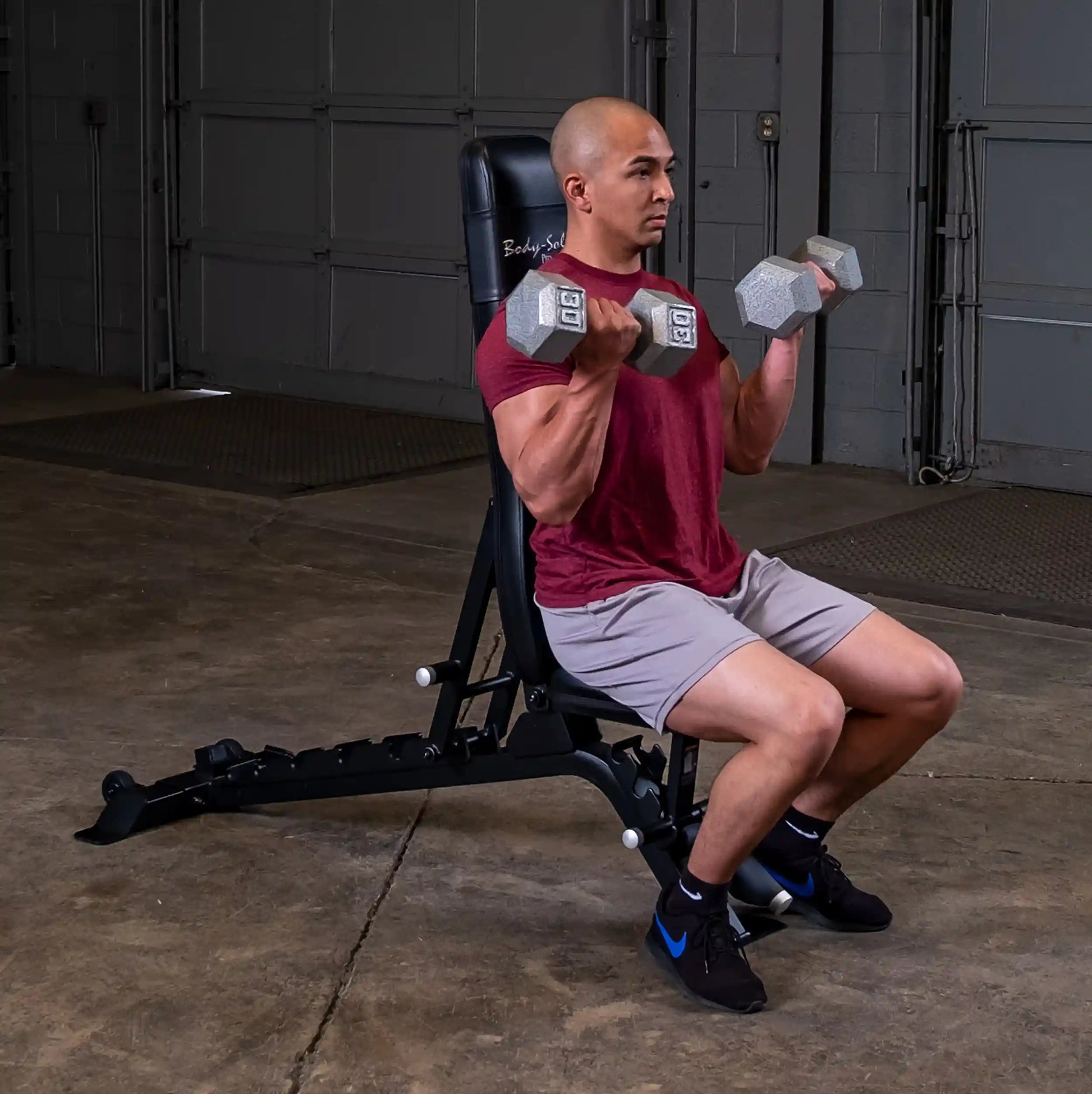 A person exercising with dumbbells while seated on the Body-Solid Pro ClubLine Adjustable Bench SFID325 in a gym setting.