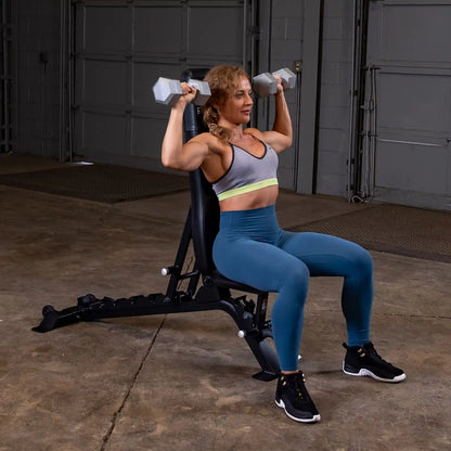 A woman performing a shoulder press exercise with dumbbells while seated on a Body-Solid Pro ClubLine Adjustable Bench SFID325 in a gym setting.
