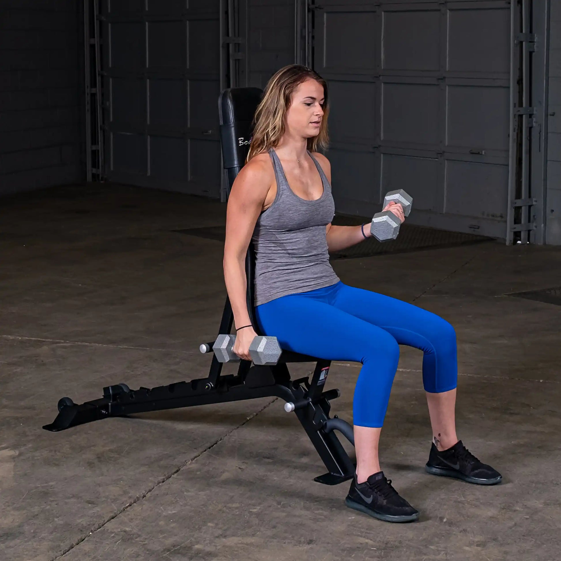 Woman performing a dumbbell exercise on the Body-Solid Pro ClubLine Adjustable Bench SFID325 in a gym setting.