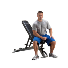 A man sitting on the Body-Solid Pro ClubLine Adjustable Bench SFID325, wearing a gray shirt and blue shorts, with a focused expression.