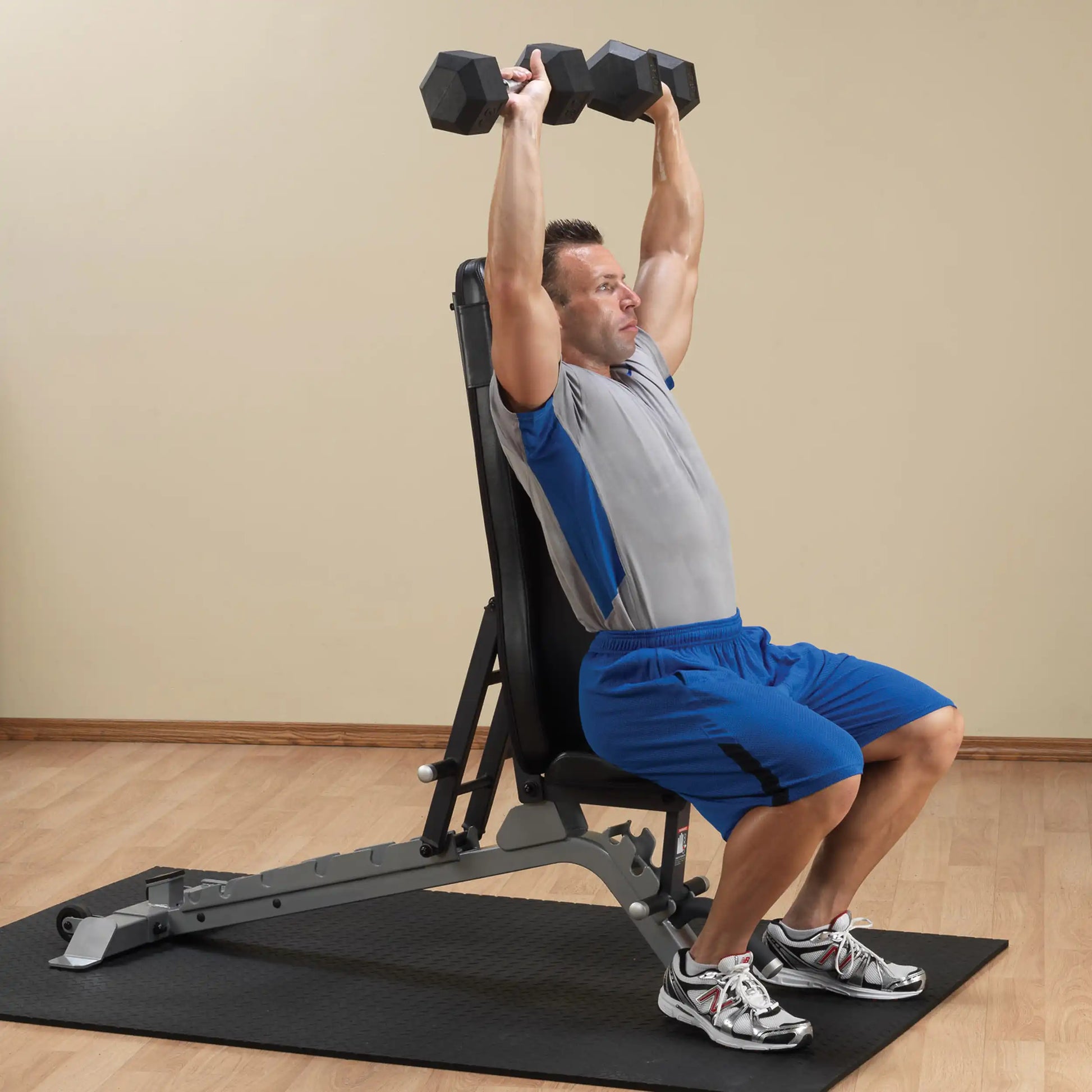 A person performing an overhead dumbbell press while seated on a Body-Solid Pro ClubLine Adjustable Bench SFID325, showcasing their workout in a fitness environment.