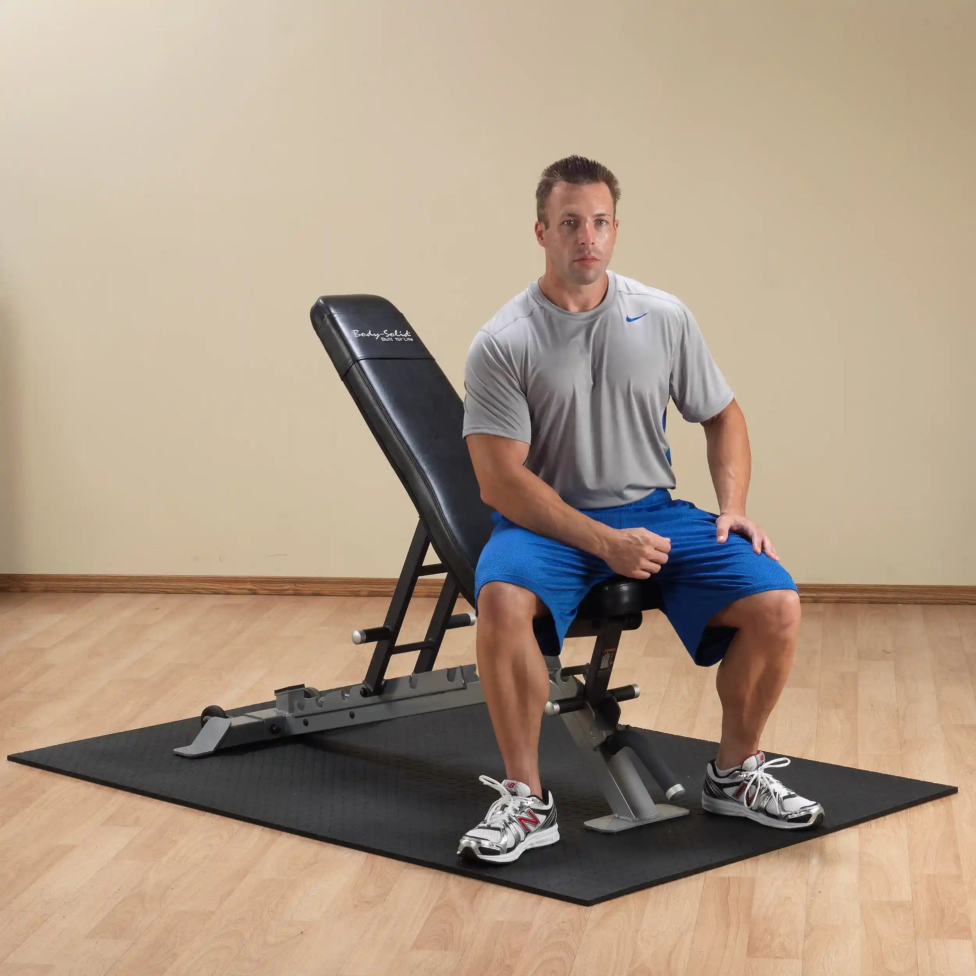 Man sitting on the Body-Solid Pro ClubLine Adjustable Bench SFID325 in a gym setting, wearing a gray shirt and blue shorts.