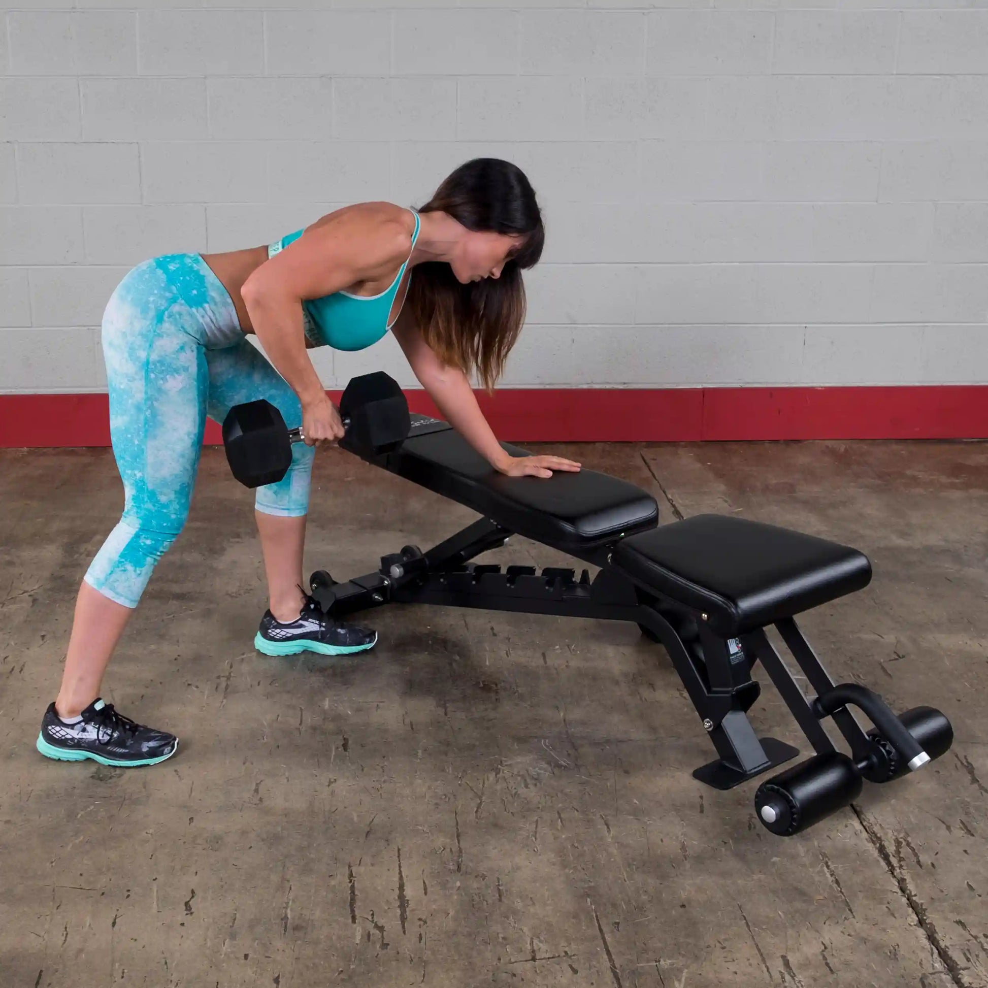 A woman performs a bent-over dumbbell row using the Body-Solid Pro ClubLine Adjustable Bench SFID425 in a gym setting.