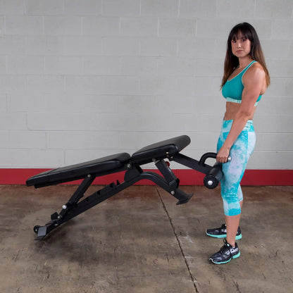 A woman in athletic wear lifting the Body-Solid Pro ClubLine Adjustable Bench SFID425 in a gym setting with a plain wall in the background.