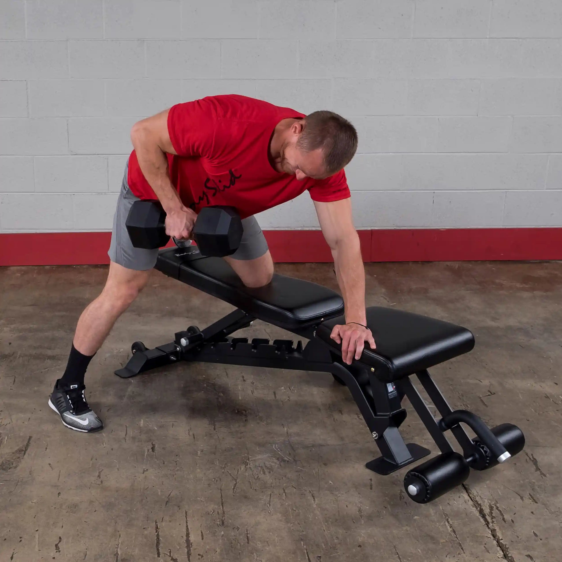 A person performing a one-arm dumbbell row on the Body-Solid Pro ClubLine Adjustable Bench SFID425 in a gym setting, showcasing proper form and technique.