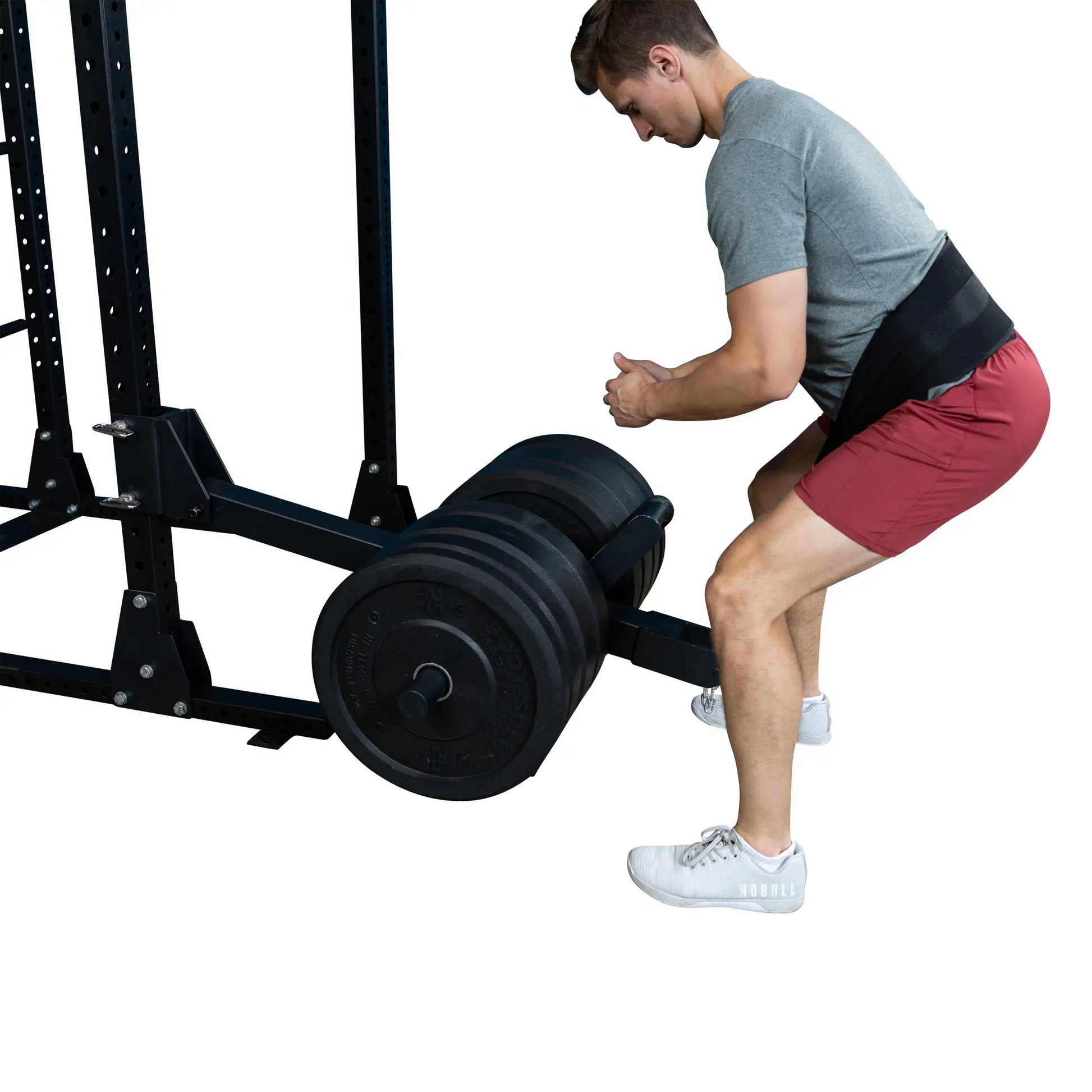 A man using the Body-Solid Pro ClubLine Belt Squat Attachment SPRBSA with a loaded barbell. He is positioned in a squatting stance, demonstrating proper form for the exercise.