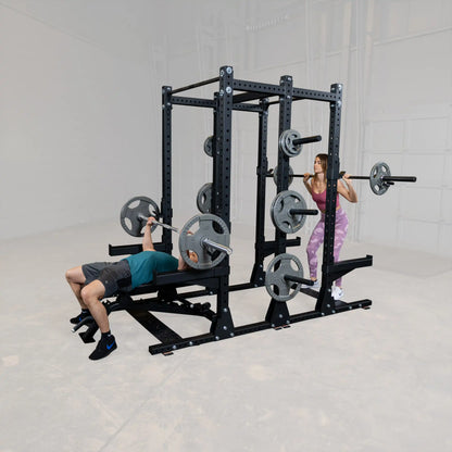 Two individuals using the Body-Solid Pro ClubLine Commercial Double Half Rack Kit SPRDBLKIT; one person is performing a bench press while the other is doing a squat, showcasing the equipment's versatility in a gym setting.