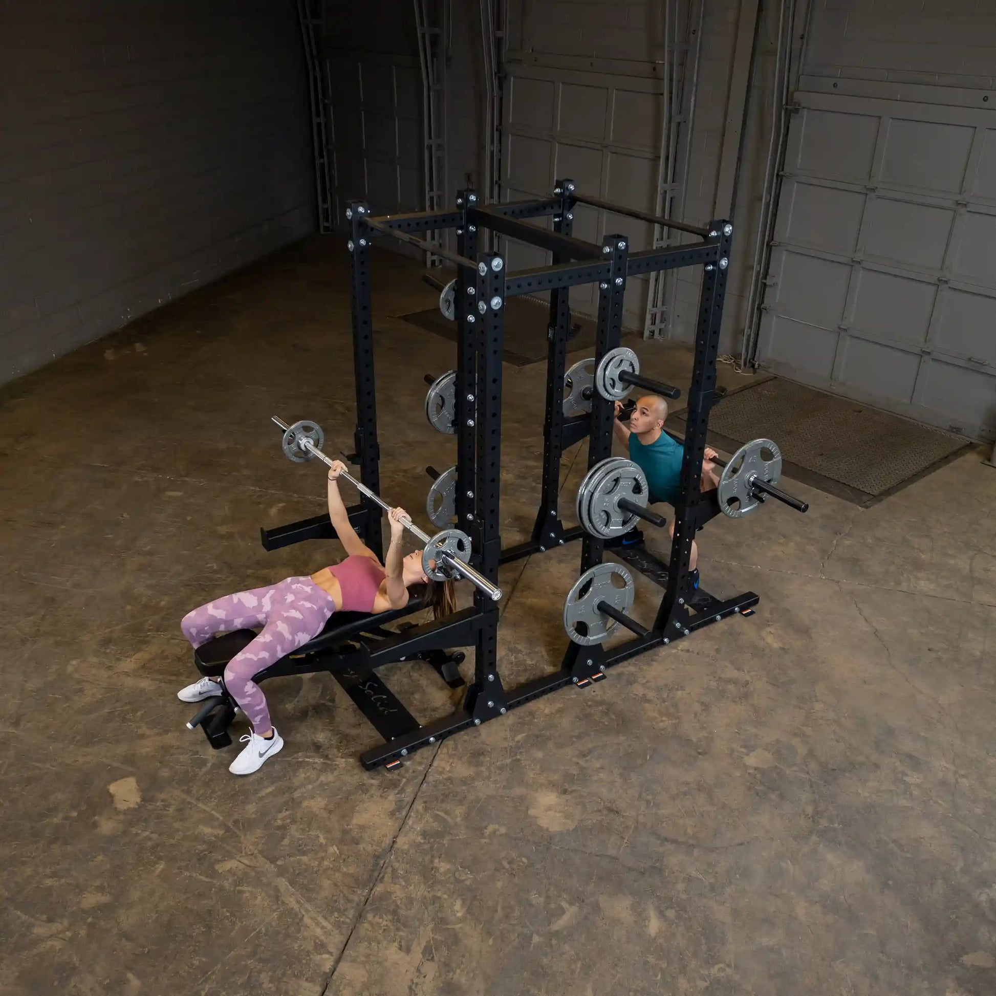 Two people working out in a gym using the Body-Solid Pro ClubLine Commercial Double Half Rack Kit SPRDBLKIT, performing exercises with barbells and weights on the rack.