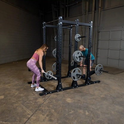 Two people exercising with a Body-Solid Pro ClubLine Commercial Double Half Rack Kit SPRDBLKIT in a gym setting.