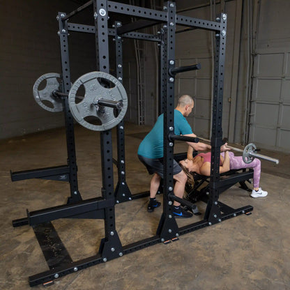 A person is spotting another person lifting weights on a bench press using the Body-Solid Pro ClubLine Commercial Double Half Rack Kit SPRDBLKIT.