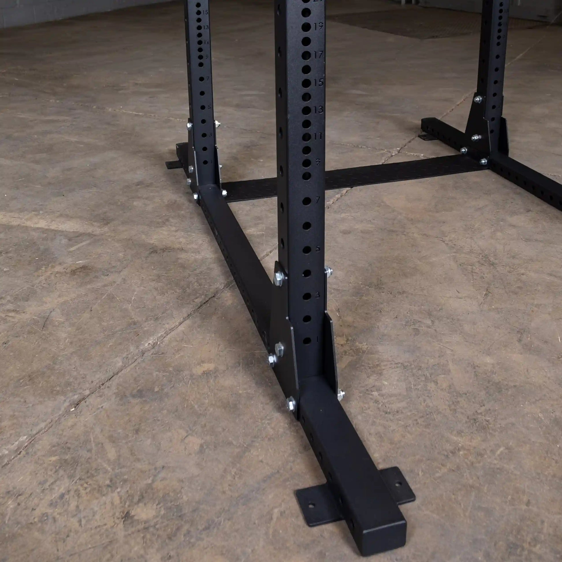 Close-up view of the base and structural details of a Body-Solid Pro ClubLine Commercial Half Rack SPR500, showing black metal construction and bolt fittings on a concrete floor.