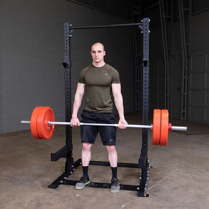 A person performing a deadlift with a barbell loaded with orange weights, standing in front of a Body-Solid Pro ClubLine Commercial Half Rack SPR500 in a gym setting.