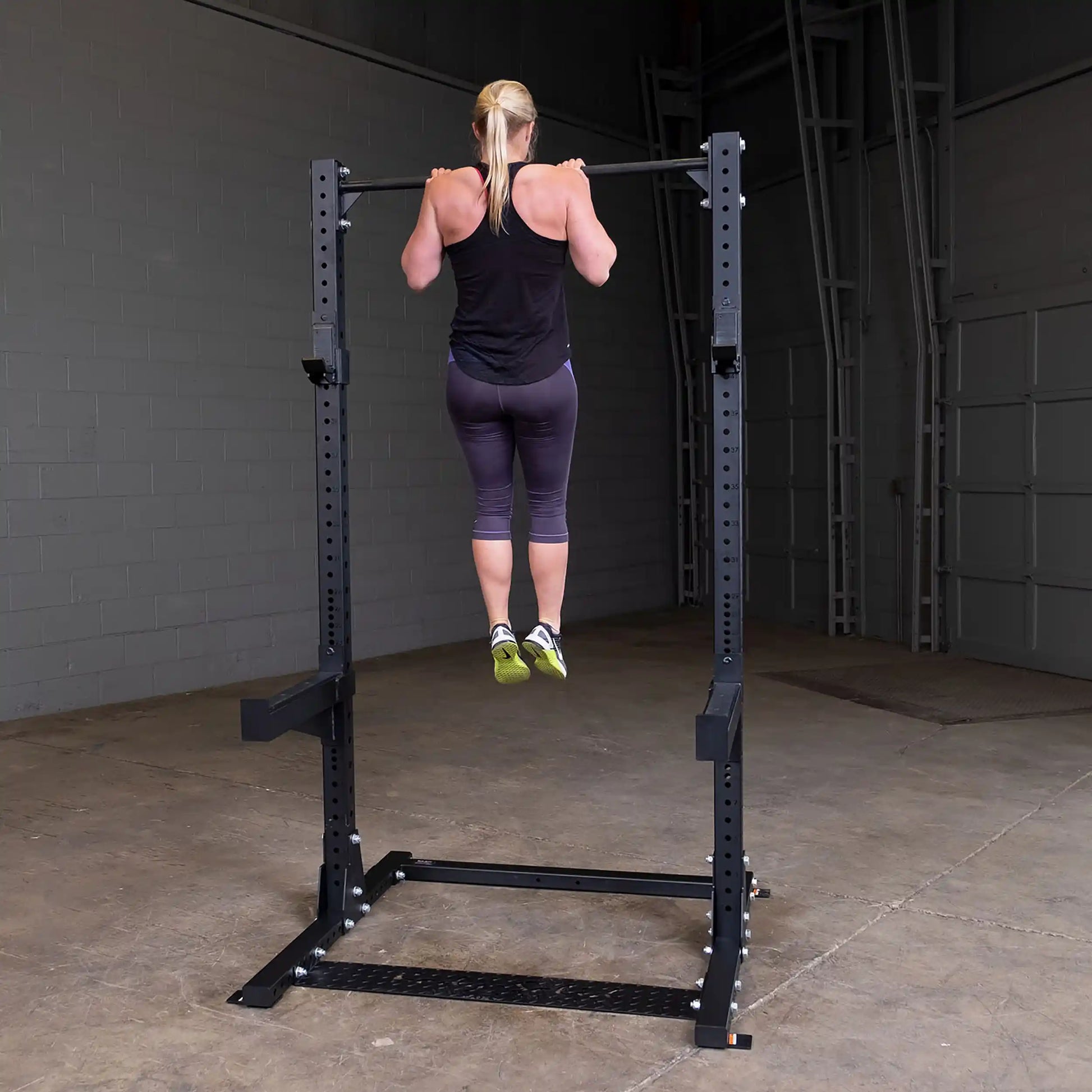 A person performing a pull-up on the Body-Solid Pro ClubLine Commercial Half Rack SPR500 in a gym setting.