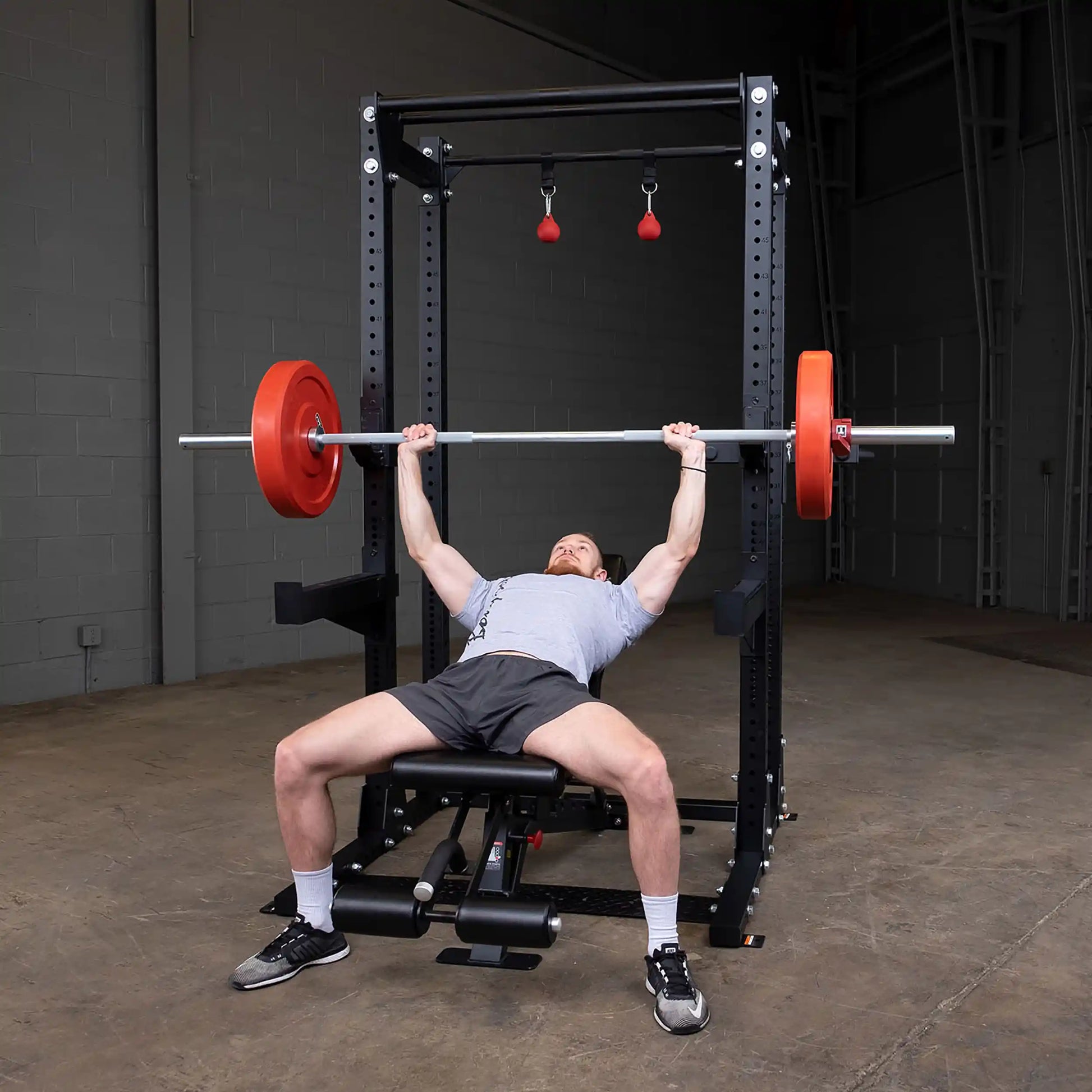 A person bench pressing with a barbell in a Body-Solid Pro ClubLine Commercial Half Rack SPR500, set in a gym environment.