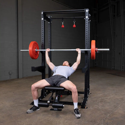 A person bench pressing with a barbell in a Body-Solid Pro ClubLine Commercial Half Rack SPR500, set in a gym environment.