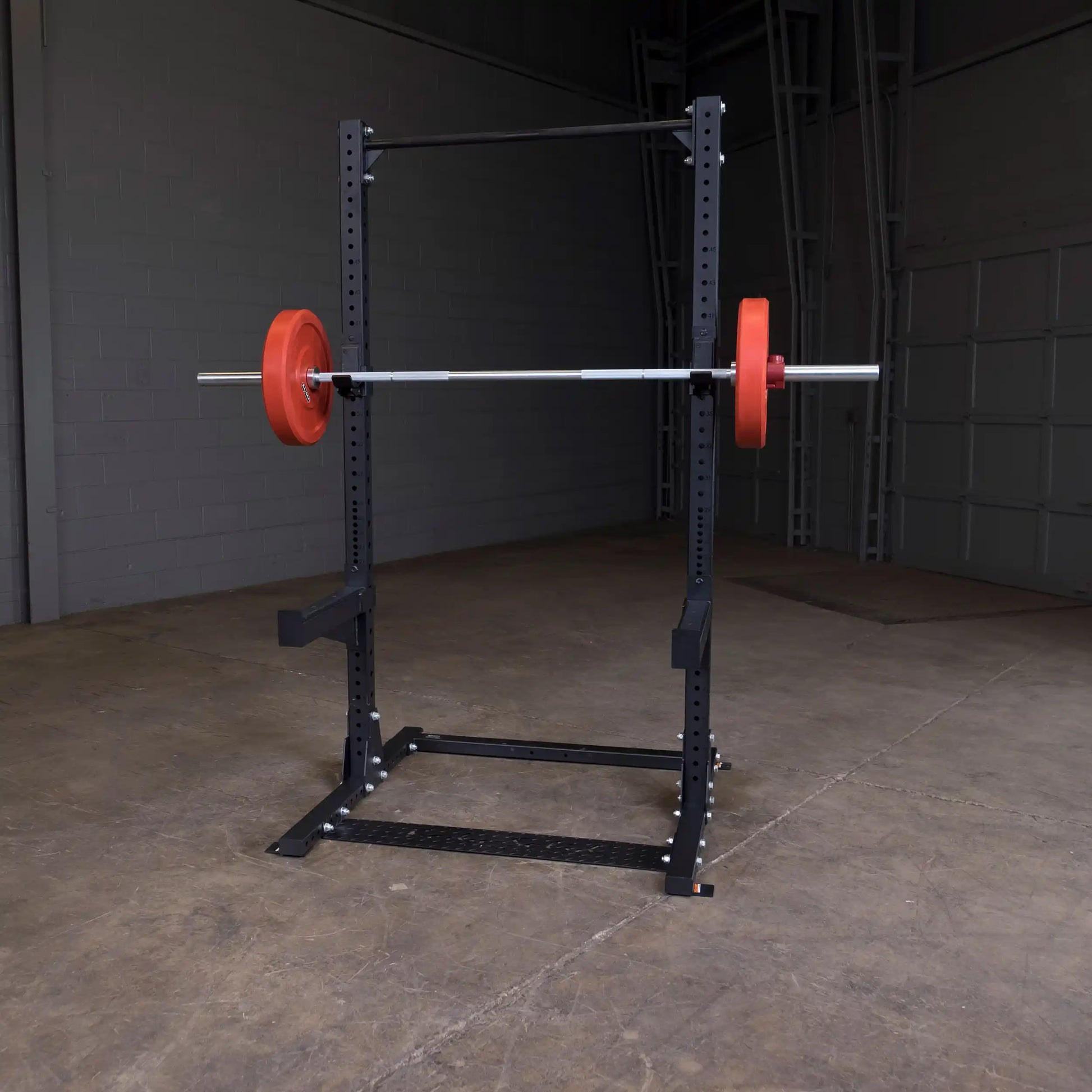 A Body-Solid Pro ClubLine Commercial Half Rack SPR500 set up in a gym setting, with a barbell and red weight plates attached.