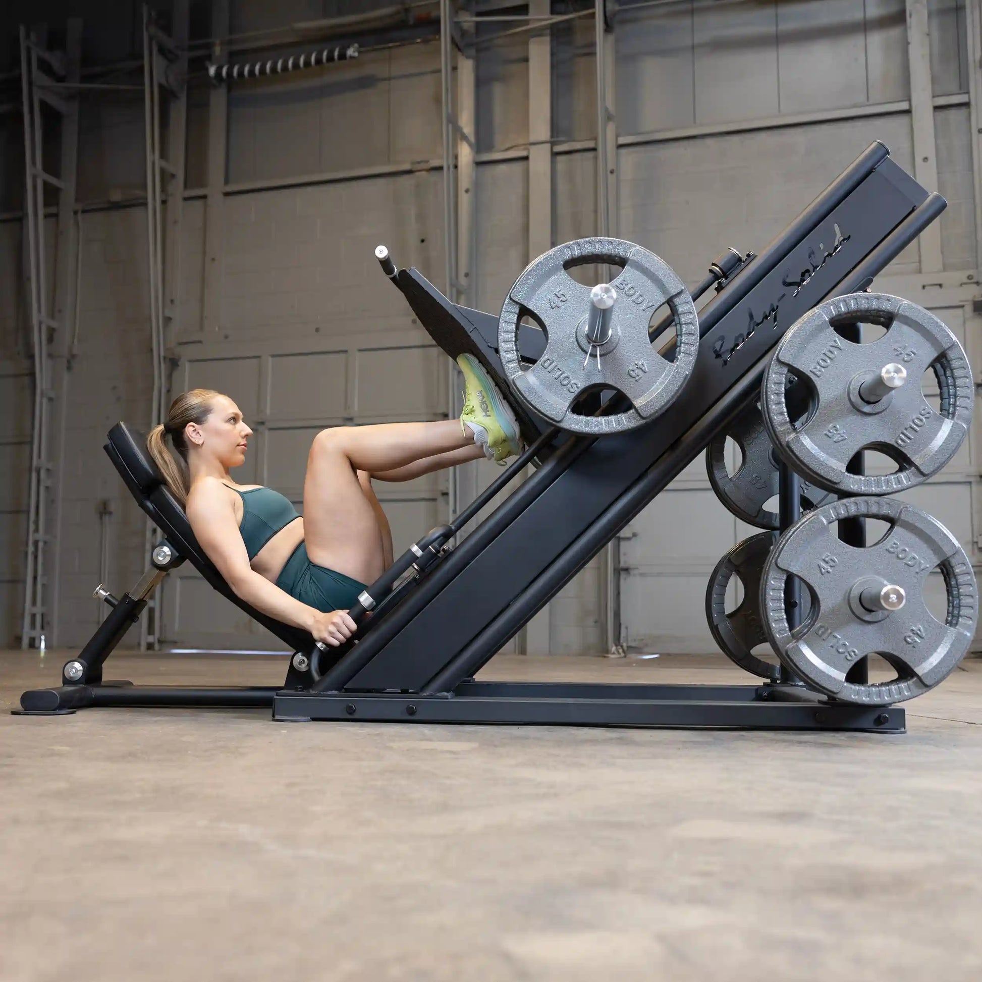 A woman using the Body-Solid Pro ClubLine Commercial Leg Press Machine SGLP500 in a gym setting, with weights on the machine.