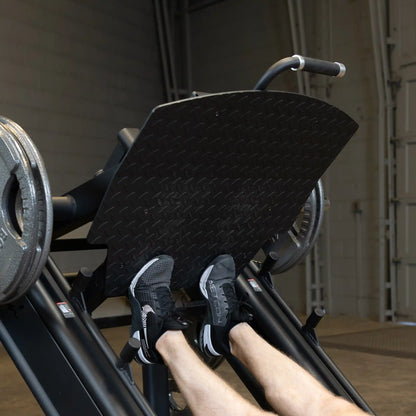 Close-up of feet on the footplate of the Body-Solid Pro ClubLine Commercial Leg Press Machine SGLP500, showcasing its design and functionality.