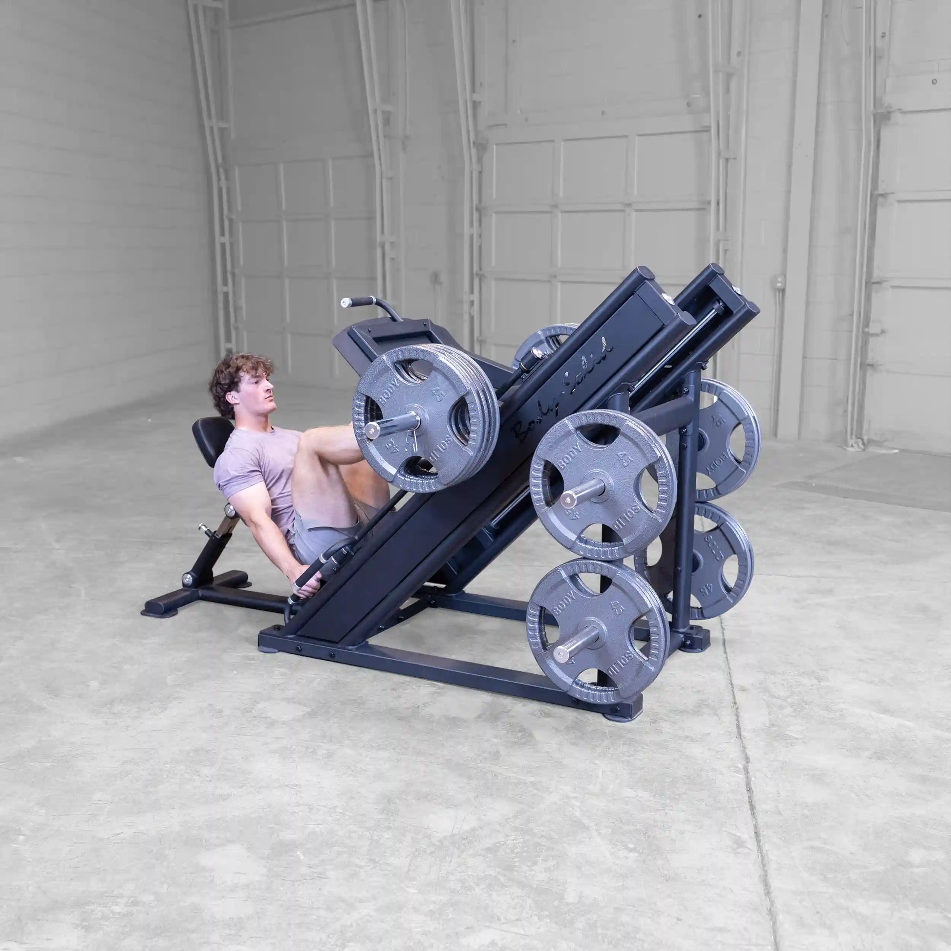 A person using the Body-Solid Pro ClubLine Commercial Leg Press Machine SGLP500, positioned at an angle with weights loaded on both sides, in a spacious gym setting.