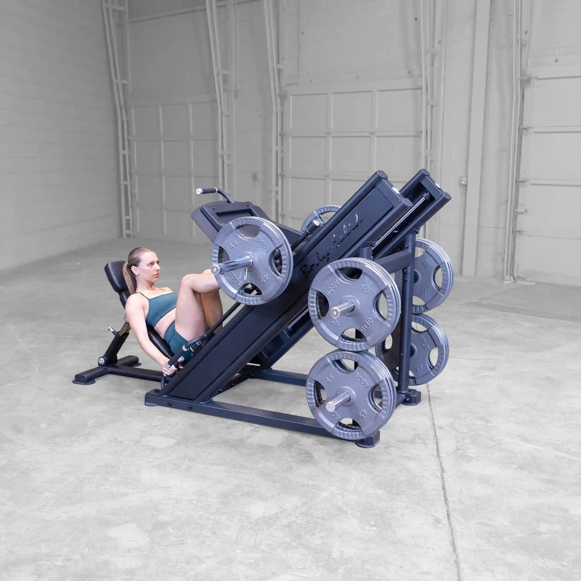 A person using the Body-Solid Pro ClubLine Commercial Leg Press Machine SGLP500 in a spacious gym setting, demonstrating leg exercises with weights loaded on the machine.