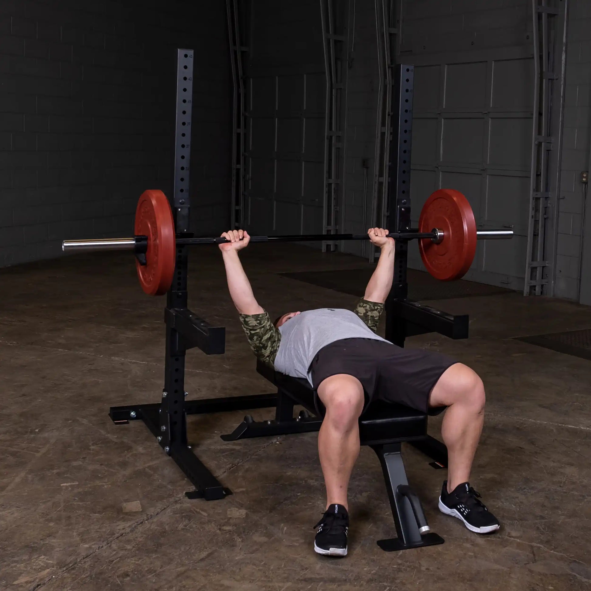 A person performing a bench press with a barbell on the Body-Solid Pro ClubLine Commercial Squat Stand SPR250 in a gym setting.