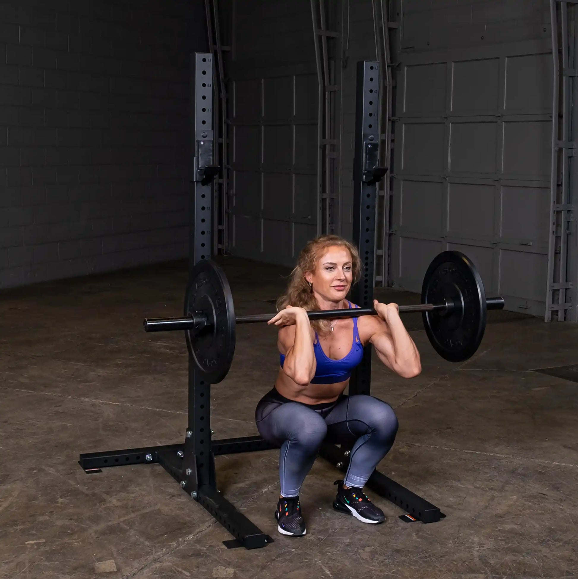 A person performing a squat with a barbell on the Body-Solid Pro ClubLine Commercial Squat Stand SPR250 in a home gym setting.