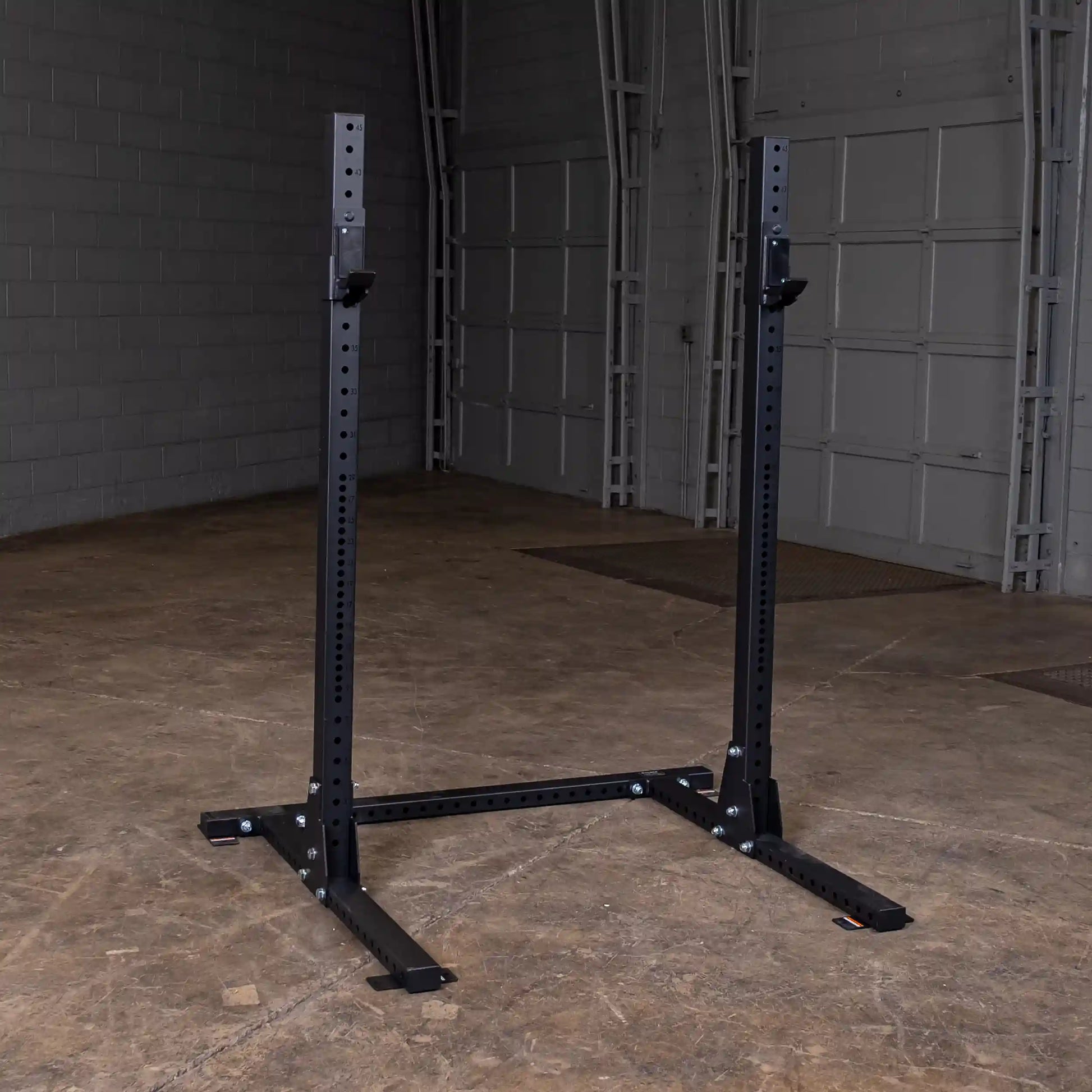 Body-Solid Pro ClubLine Commercial Squat Stand SPR250 standing in a spacious industrial-style room with concrete floors and gray brick walls.