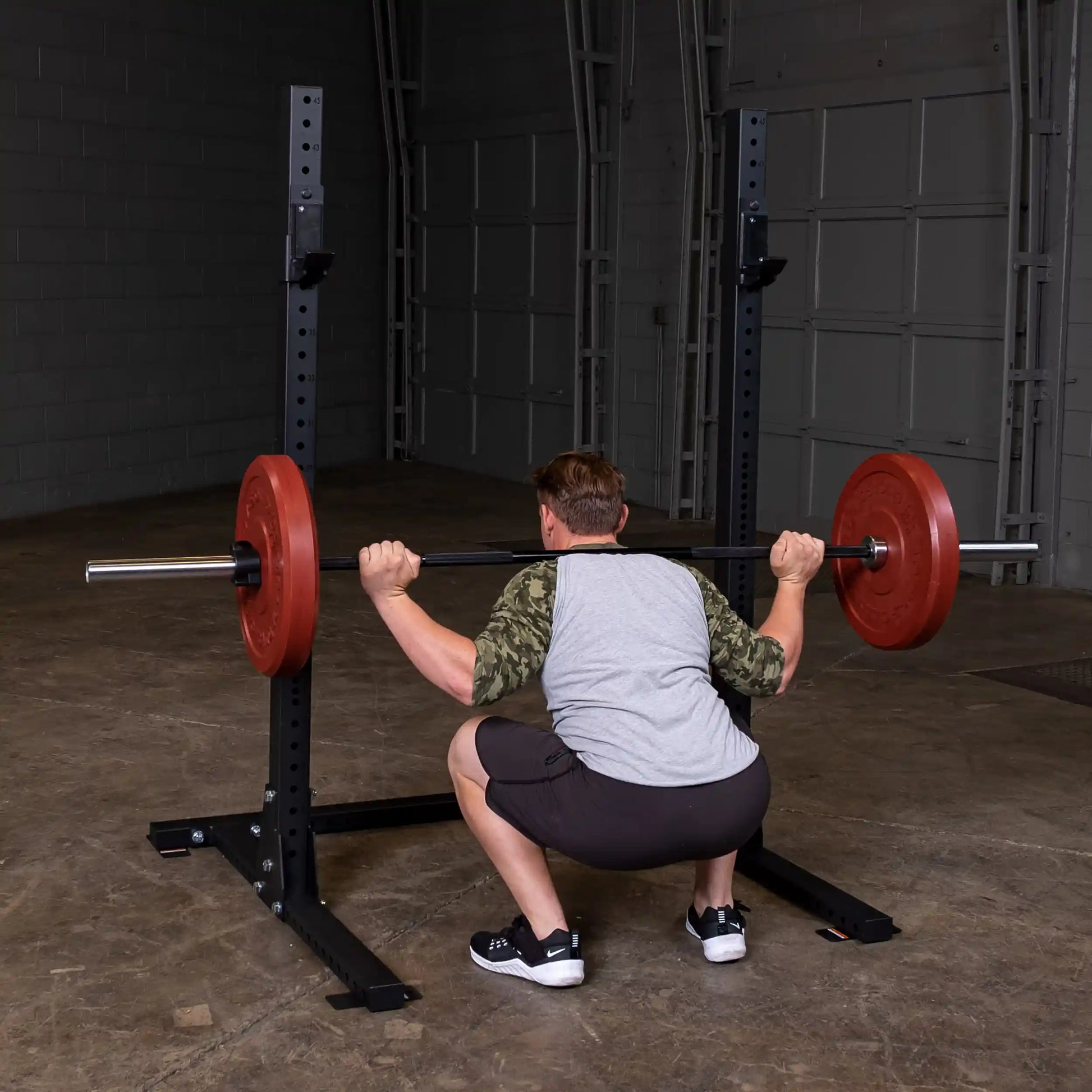 A person performing a squat with a barbell on the Body-Solid Pro ClubLine Commercial Squat Stand SPR250 in a gym setting.