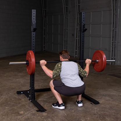 A person performing a squat with a barbell on the Body-Solid Pro ClubLine Commercial Squat Stand SPR250 in a gym setting.