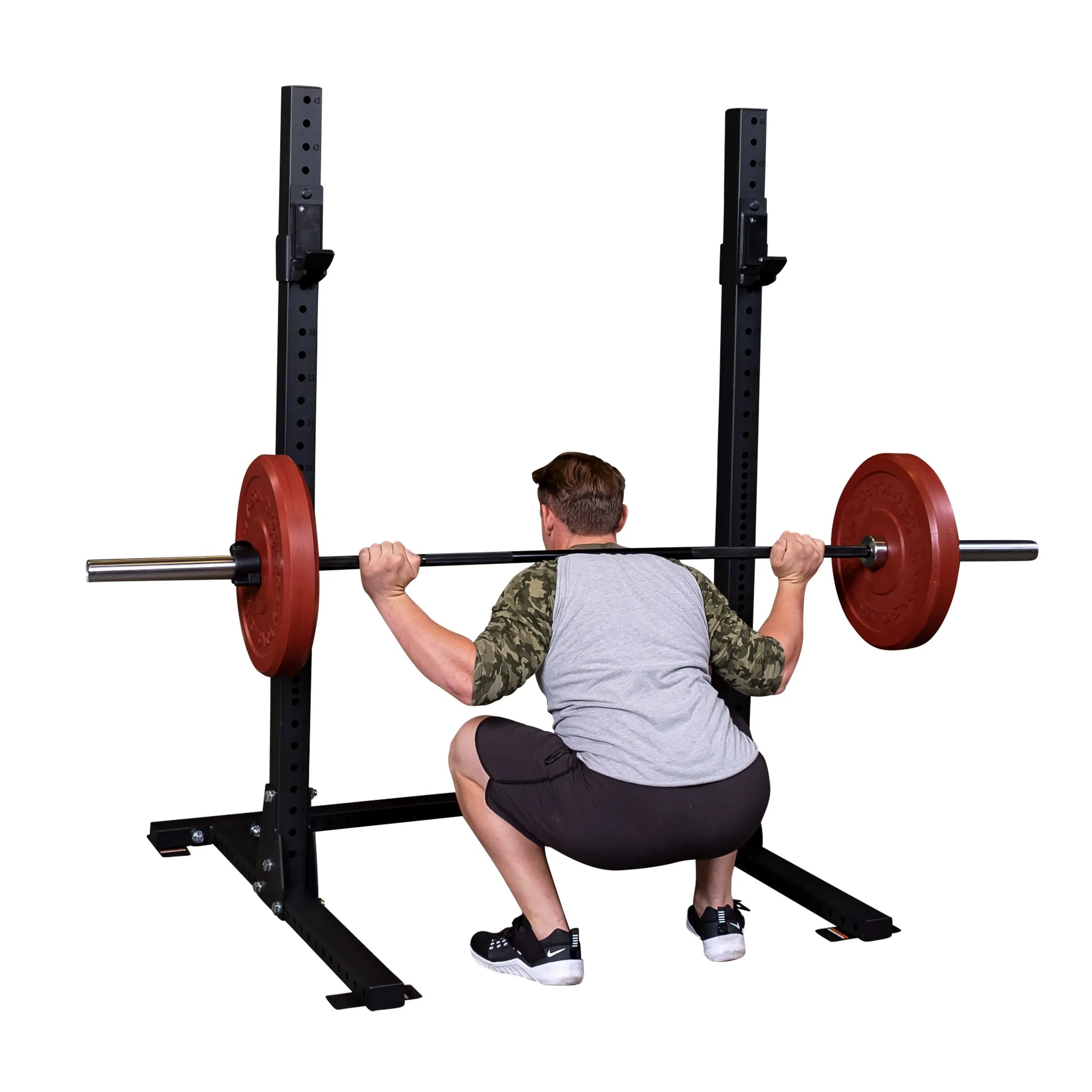 A person performing a squat while using the Body-Solid Pro ClubLine Commercial Squat Stand SPR250 with a barbell loaded with red weight plates.