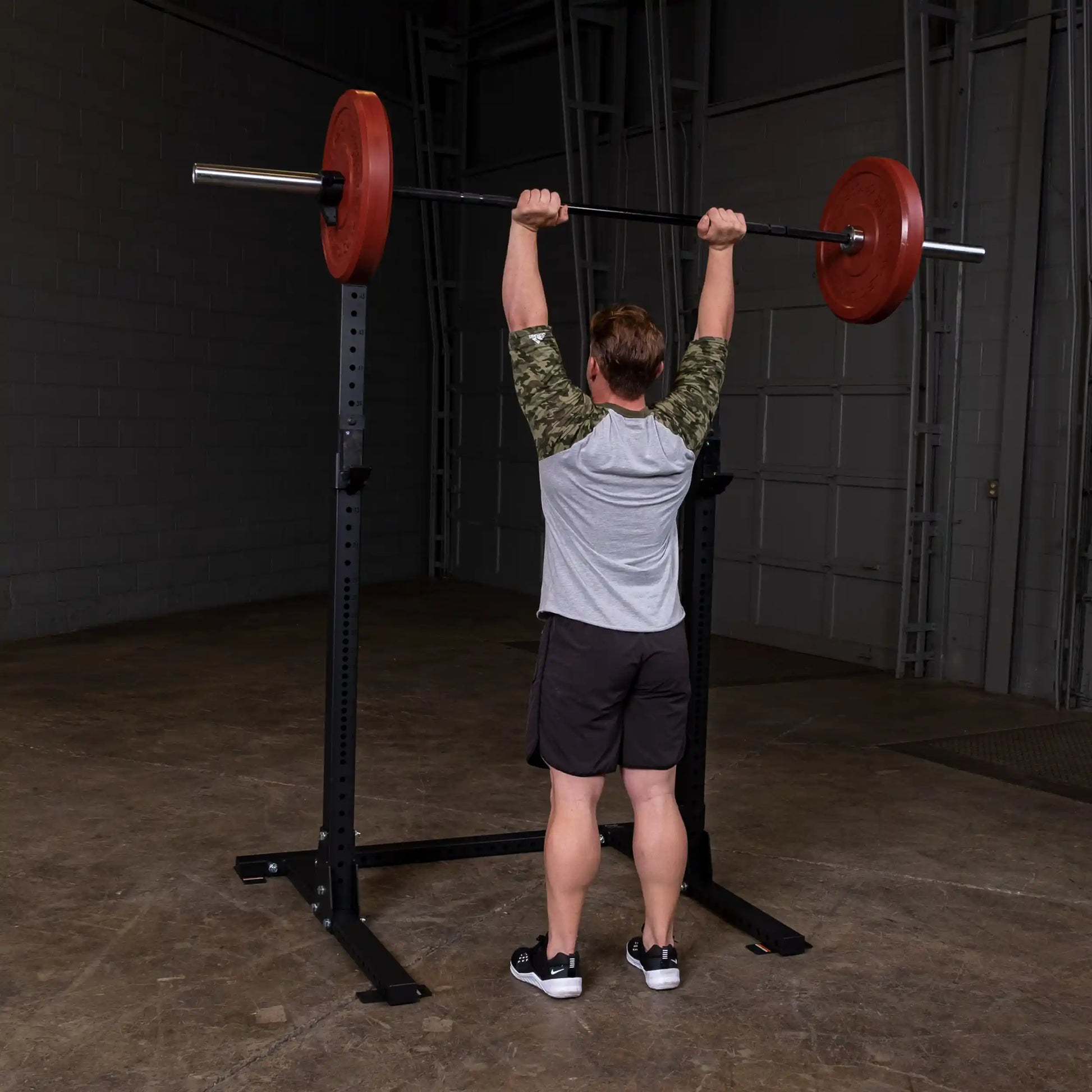 A person lifting a barbell with red weights on a Body-Solid Pro ClubLine Commercial Squat Stand SPR250 in a gym setting.
