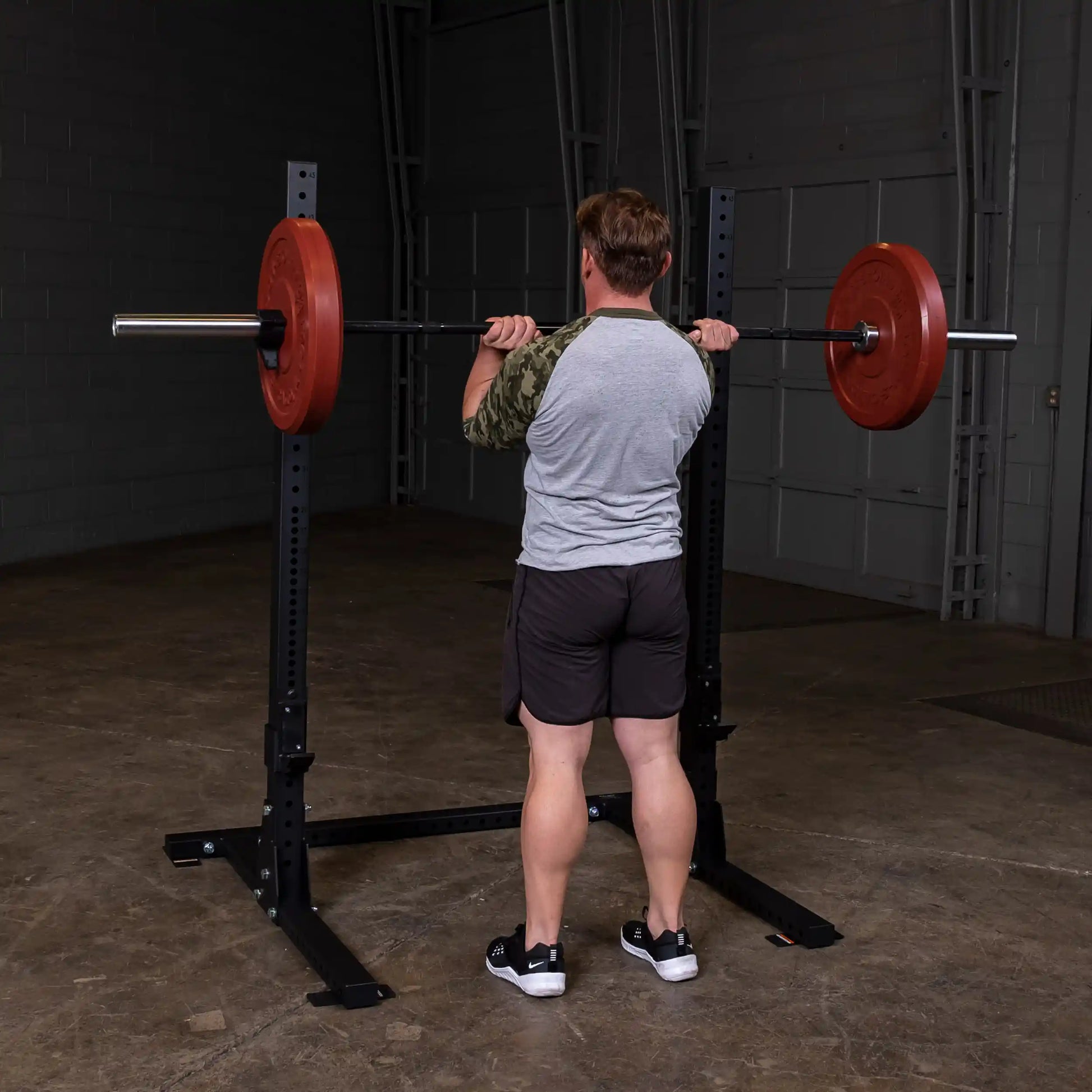 A person performing a squat with a barbell on a Body-Solid Pro ClubLine Commercial Squat Stand SPR250 in a gym setting.