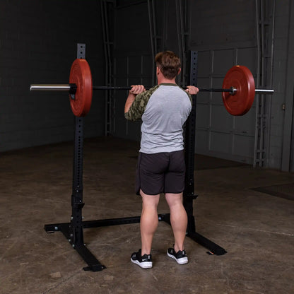 A person performing a squat with a barbell on a Body-Solid Pro ClubLine Commercial Squat Stand SPR250 in a gym setting.