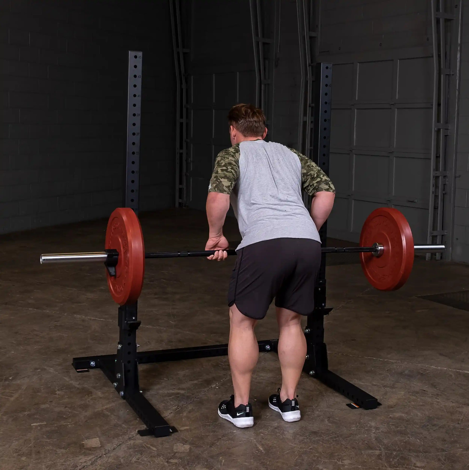 A person performing a bent-over row using a barbell with red weights on the Body-Solid Pro ClubLine Commercial Squat Stand SPR250 in a gym setting.