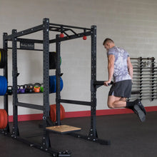 A person performing a dip exercise using the Body-Solid Pro ClubLine Dip Station Attachment SPRDIP, with colorful weight plates and kettlebells in the background.
