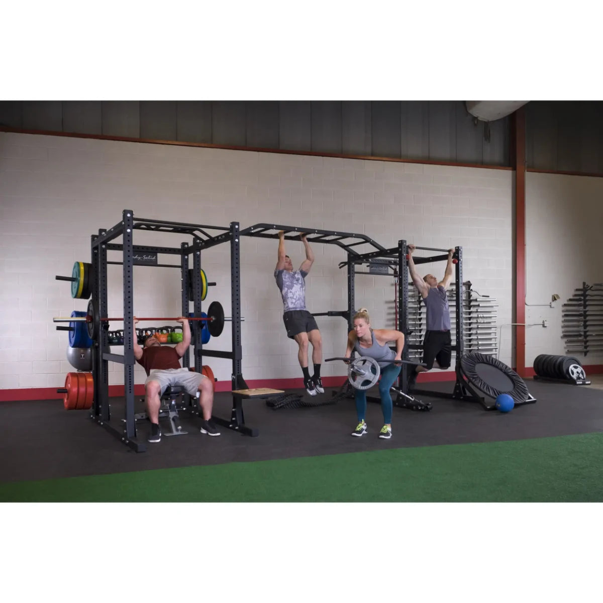 Four people exercising using the Body-Solid Pro ClubLine Double Extended Commercial Power Rack SPR1000DBBACK in a gym setting, surrounded by weights and fitness equipment.