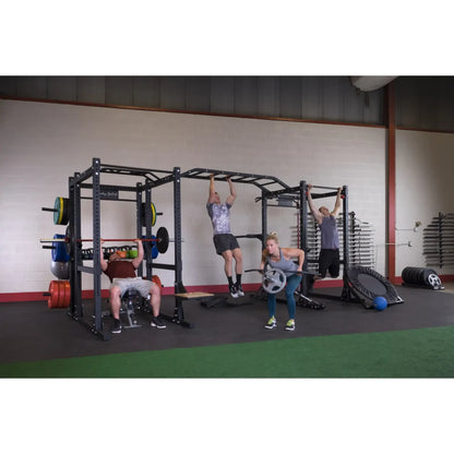 Four people exercising using the Body-Solid Pro ClubLine Double Extended Commercial Power Rack SPR1000DBBACK in a gym setting, surrounded by weights and fitness equipment.
