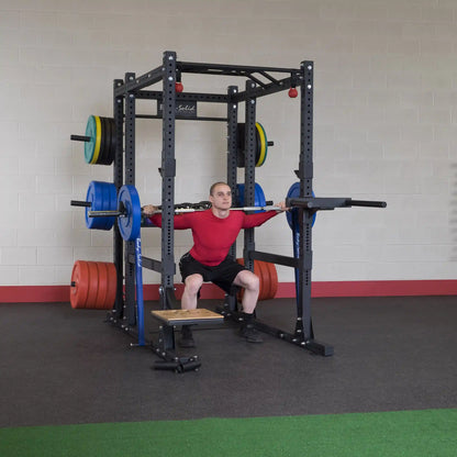 A person performing a squat with a barbell on a Body-Solid Pro ClubLine Extended Commercial Power Rack SPR1000BACK, equipped with multiple weight plates in a gym setting.