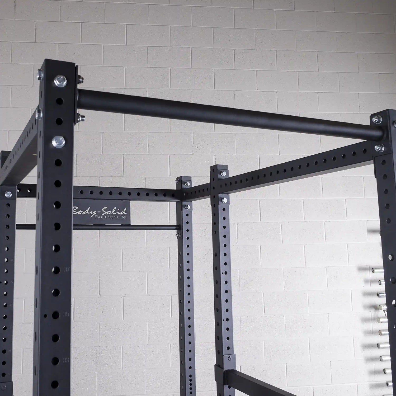 Close-up of a Body-Solid power rack, featuring a sturdy black frame with adjustable height settings and a horizontal bar, set against a light-colored wall.