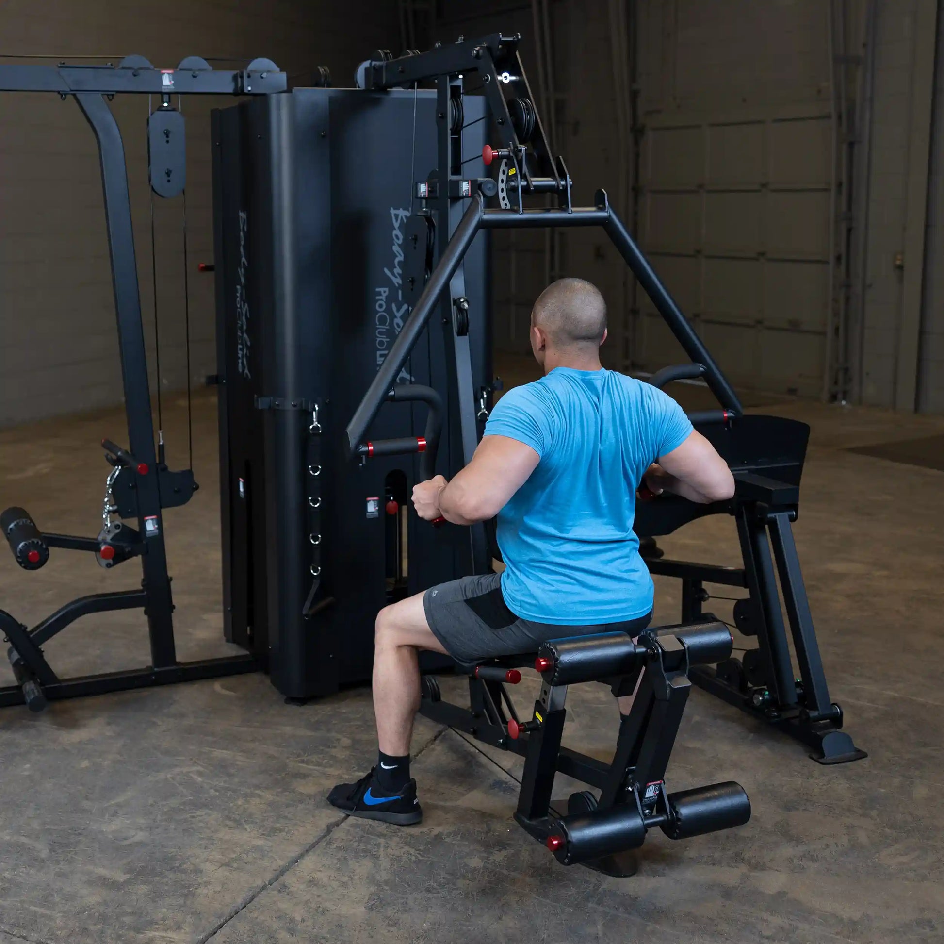 A person using the Body-Solid Pro ClubLine Four-Stack Gym S1000, performing a seated exercise in a spacious gym environment.