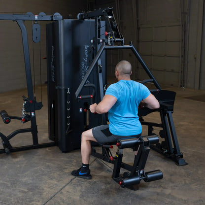 A person using the Body-Solid Pro ClubLine Four-Stack Gym S1000, performing a seated exercise in a spacious gym environment.