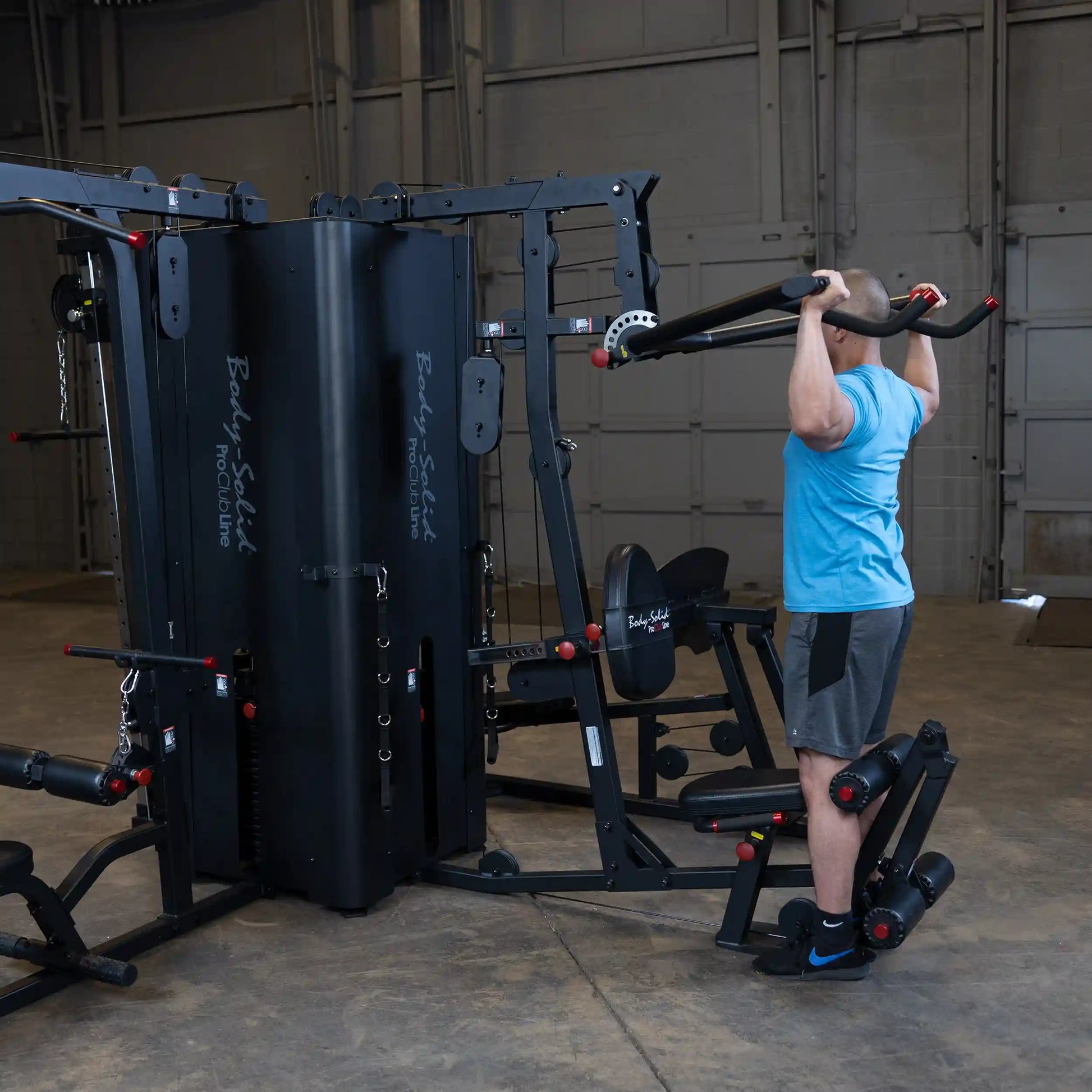 A person performing an exercise on the Body-Solid Pro ClubLine Four-Stack Gym S1000, featuring multiple weight stacks and various attachments in a spacious gym environment.