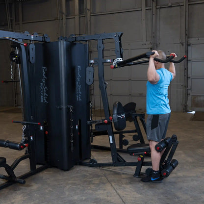 A person performing an exercise on the Body-Solid Pro ClubLine Four-Stack Gym S1000, featuring multiple weight stacks and various attachments in a spacious gym environment.