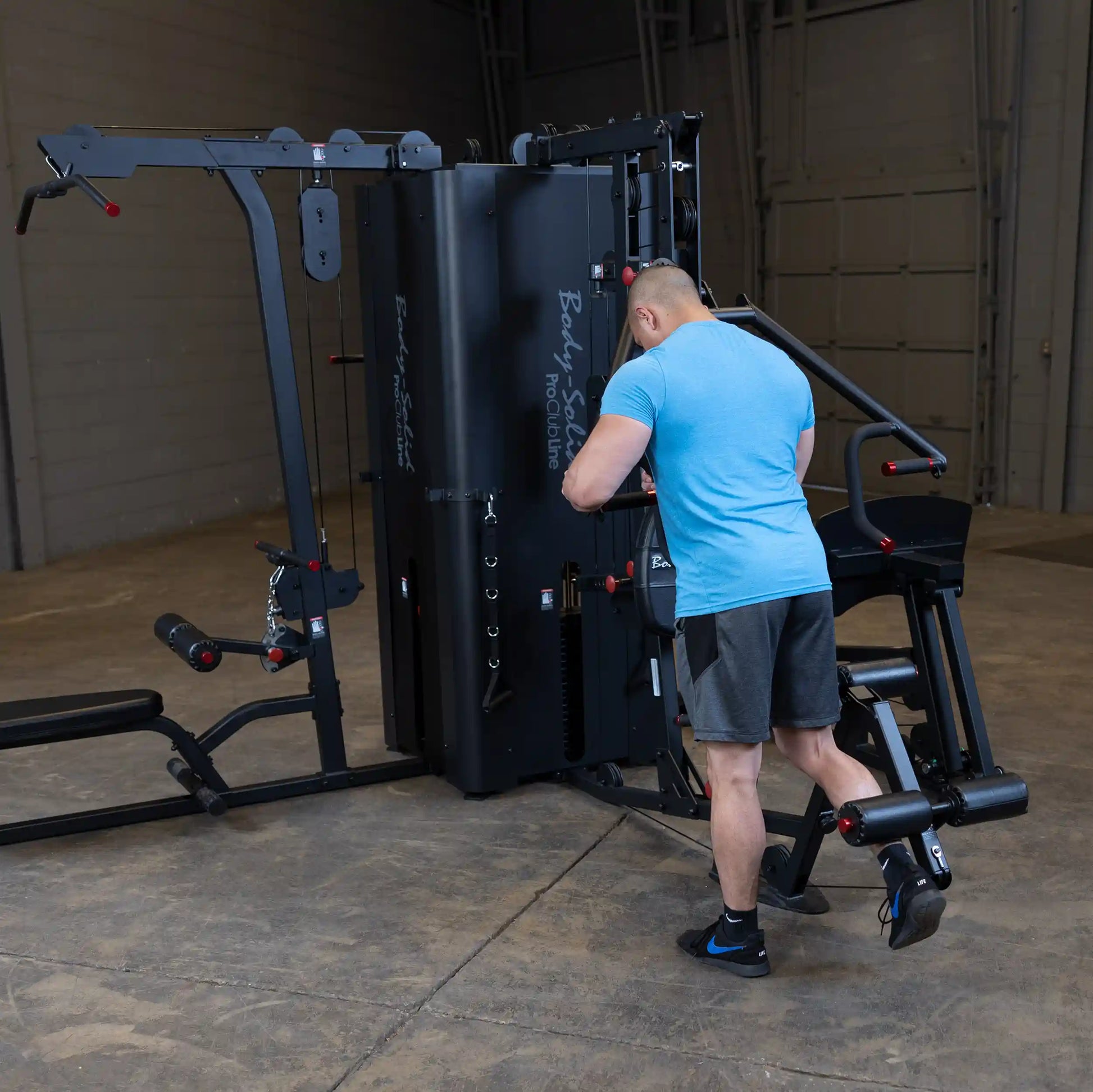 A person using the Body-Solid Pro ClubLine Four-Stack Gym S1000 in a spacious gym setting, focusing on an exercise station.