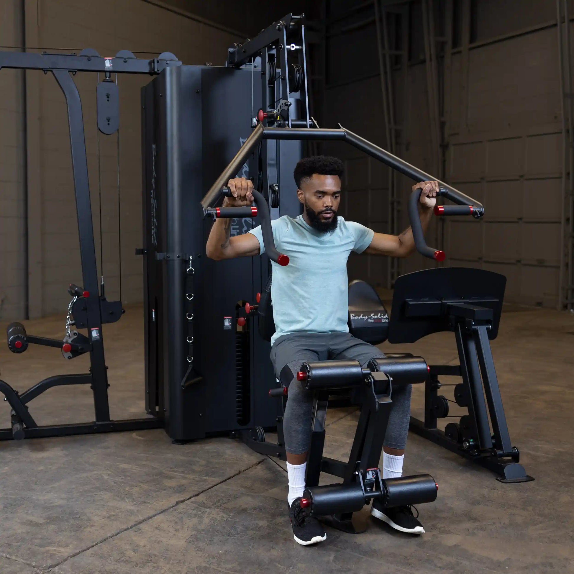 A person using the Body-Solid Pro ClubLine Four-Stack Gym S1000, performing an exercise while seated in a fitness facility.