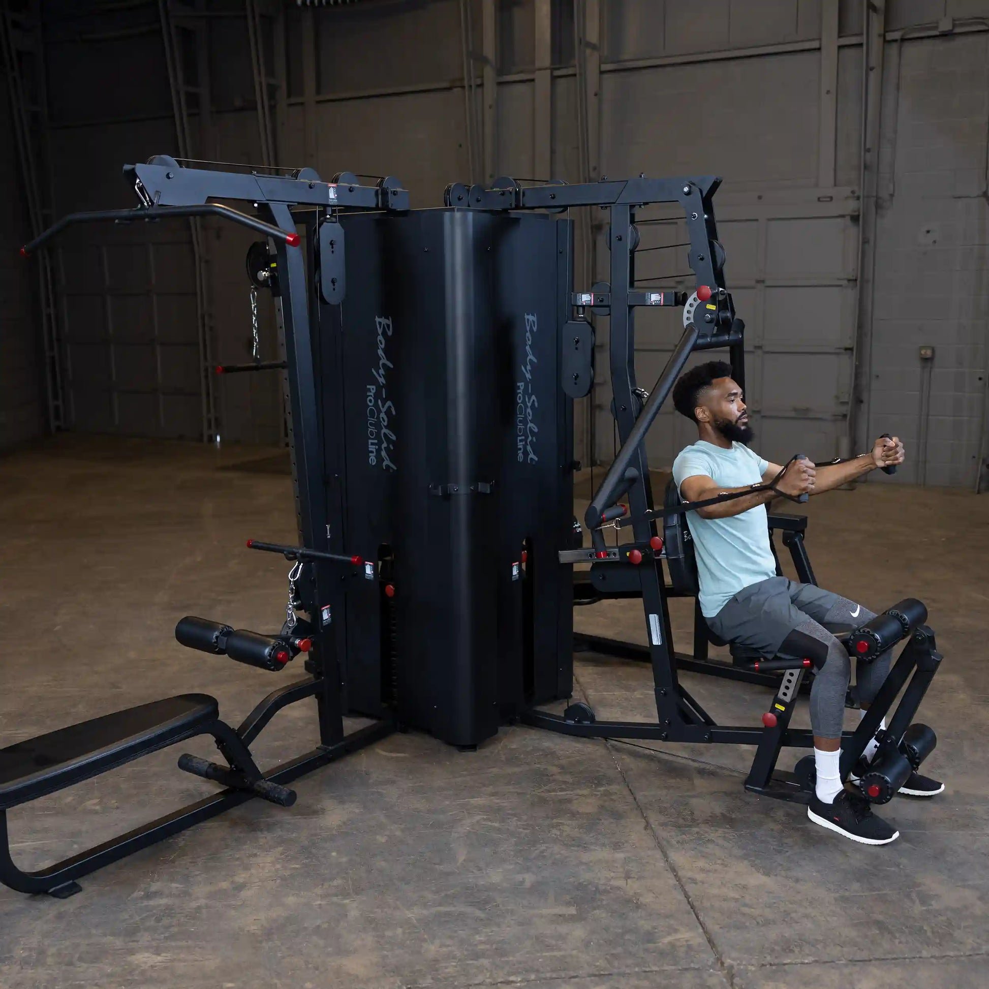 A man using the Body-Solid Pro ClubLine Four-Stack Gym S1000 in a spacious gym environment, demonstrating various workout exercises on the equipment.