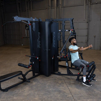 A man using the Body-Solid Pro ClubLine Four-Stack Gym S1000 in a spacious gym environment, demonstrating various workout exercises on the equipment.