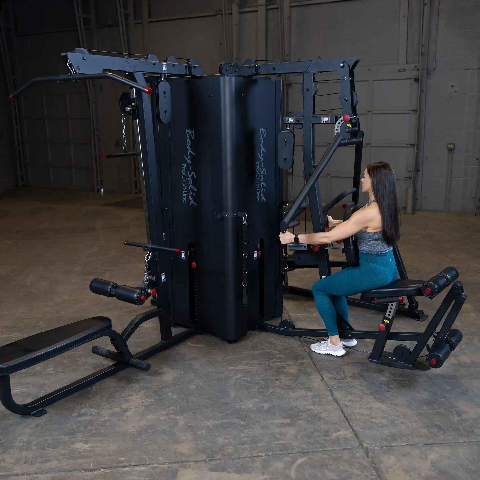 A woman using the Body-Solid Pro ClubLine Four-Stack Gym S1000 in a spacious gym setting, demonstrating a seated exercise with the equipment.
