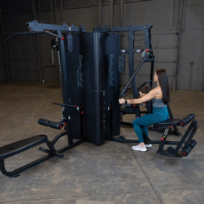 A woman using the Body-Solid Pro ClubLine Four-Stack Gym S1000 in a spacious gym setting, demonstrating a seated exercise with the equipment.